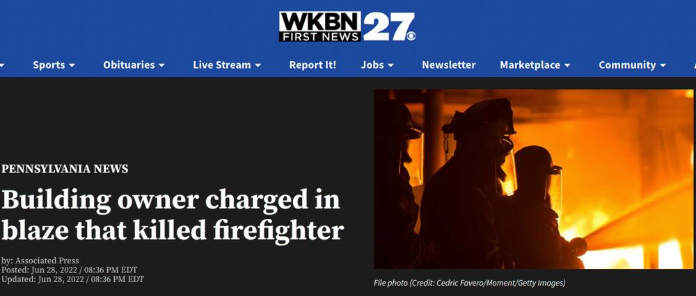 Silhouette of emergency responders working at a building fire scene with intense orange flames glowing at night.