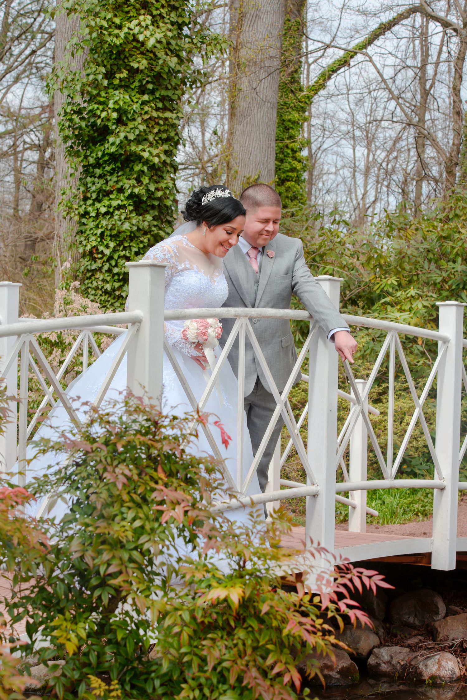 A couple shares a romantic moment together on a white wooden bridge in a garden setting full of greenery.