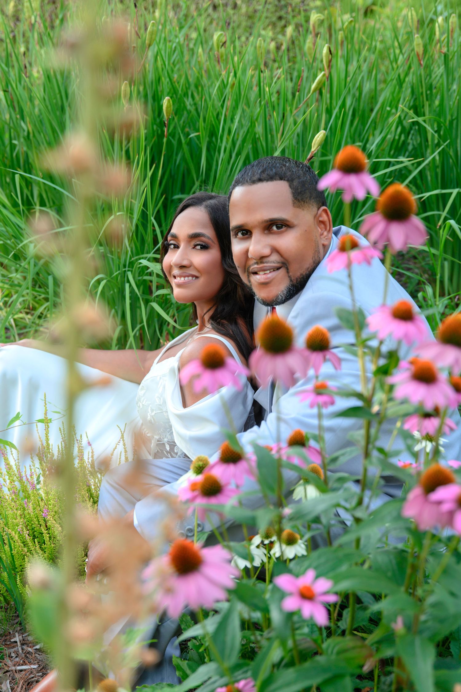 A couple poses together in a garden with pink coneflowers and tall grass on a summer day.