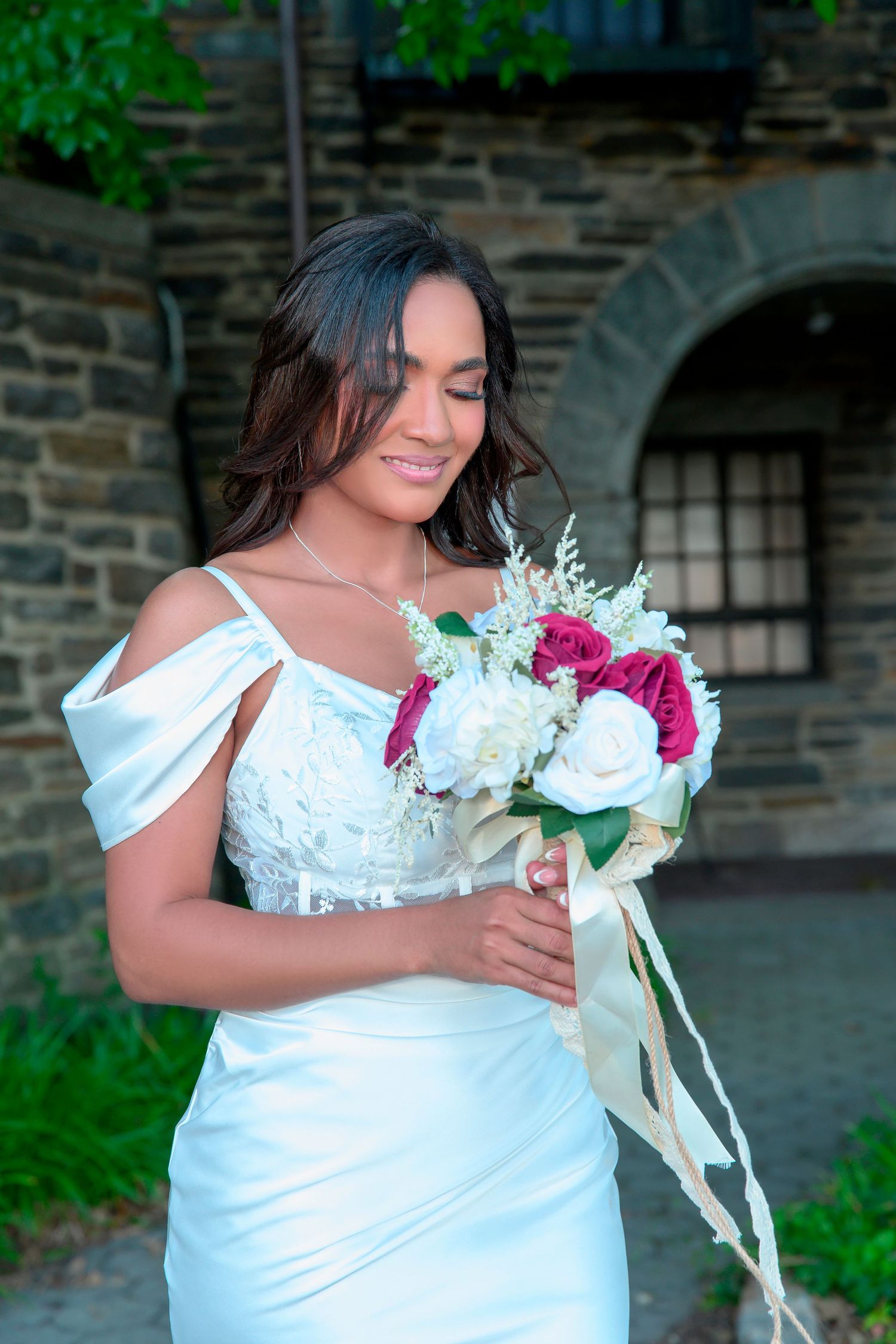 A bride in an elegant white off-shoulder wedding dress holds a vibrant bouquet of pink and white flowers.