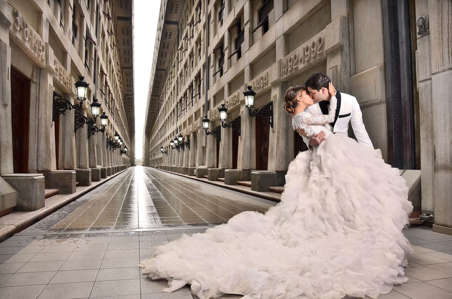 A romantic wedding couple embraces in an elegant colonnade corridor with dramatic perspective and a flowing white gown.