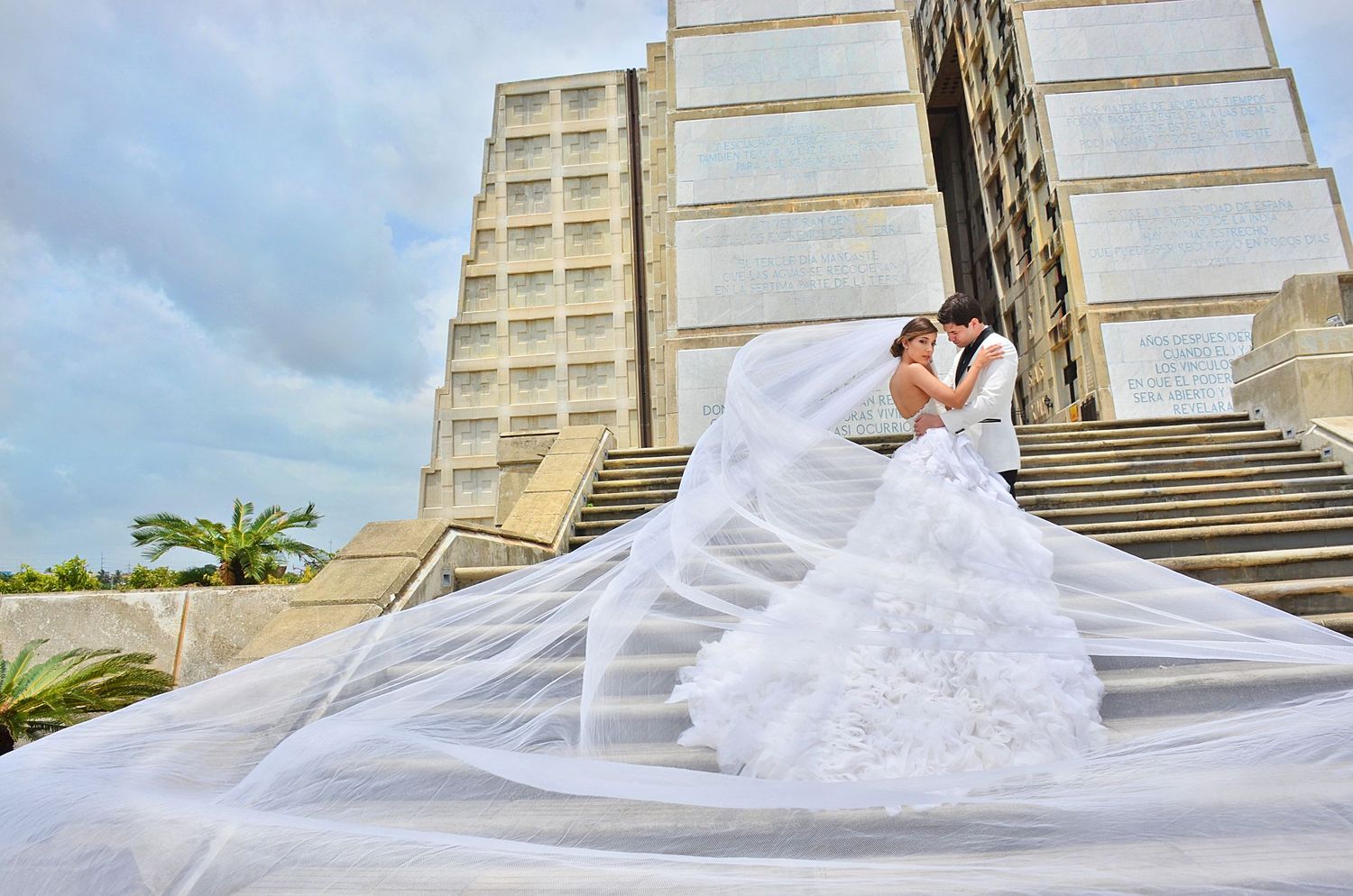 A dramatic wedding photograph captured on grand stone steps with a flowing white gown and veil against modern architecture.