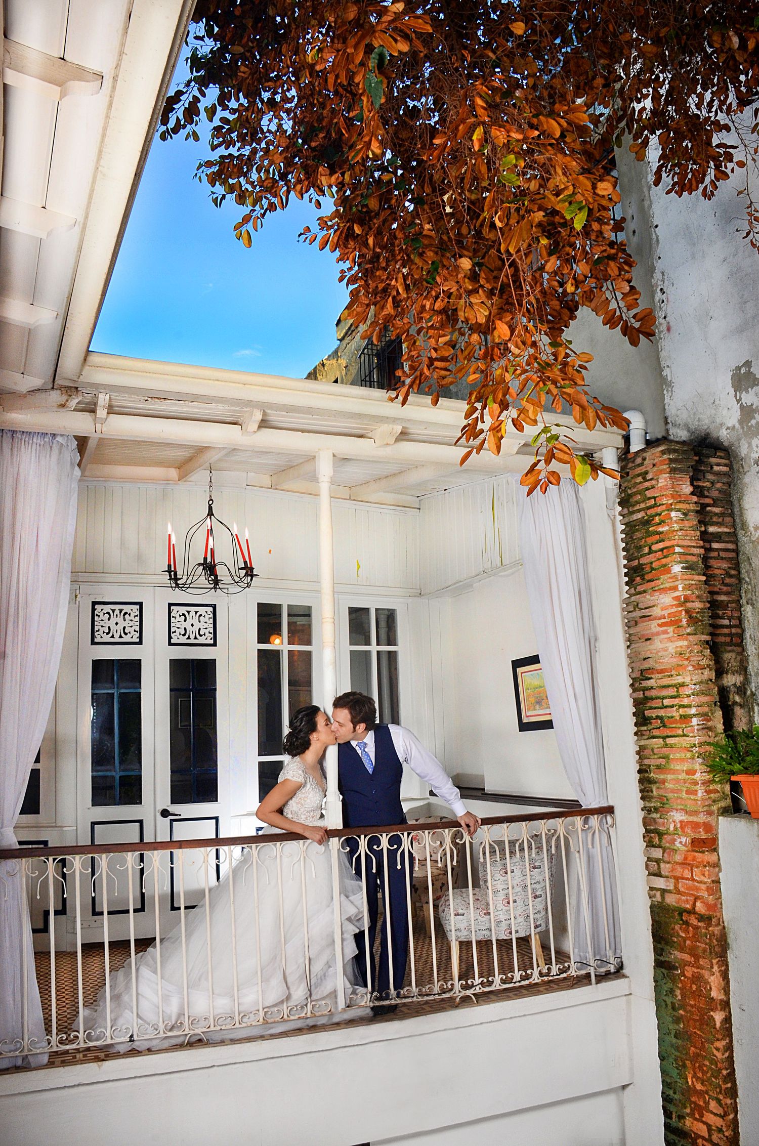 A romantic wedding scene on a white balcony with autumn leaves framing the view.