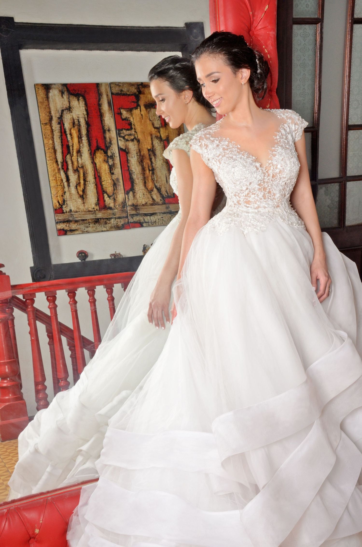 Wedding dress with delicate lace bodice and flowing layered skirt displayed against a red and white backdrop.