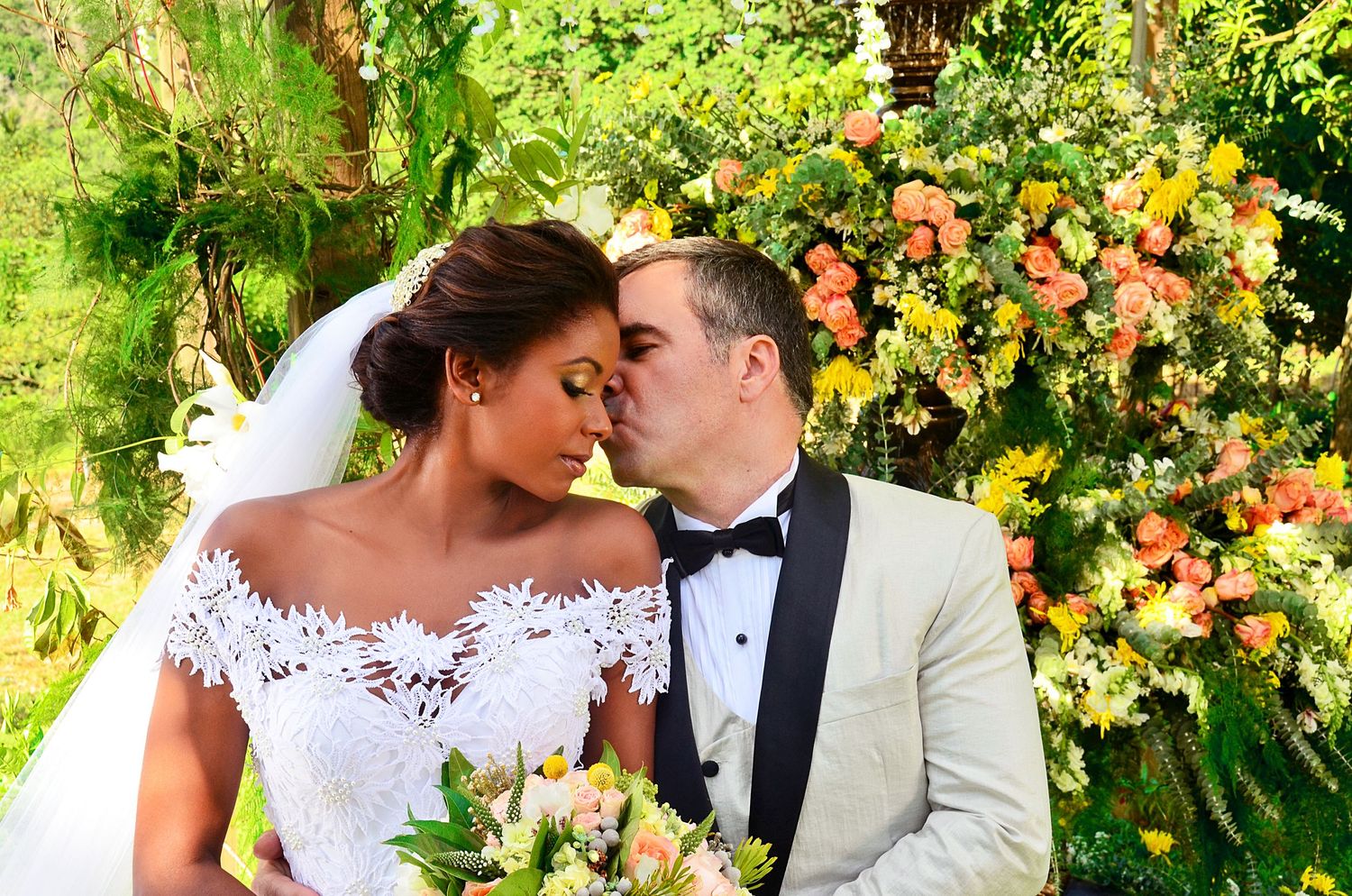 Newlyweds share a romantic moment in front of a colorful floral garden display.