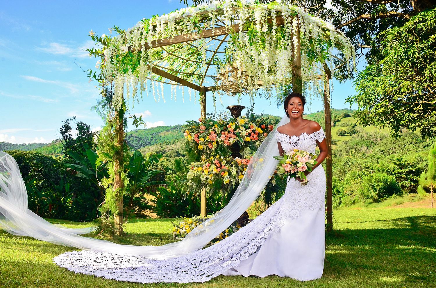 Wedding portrait under romantic floral arbor with cascading white wisteria and mountain landscape backdrop.