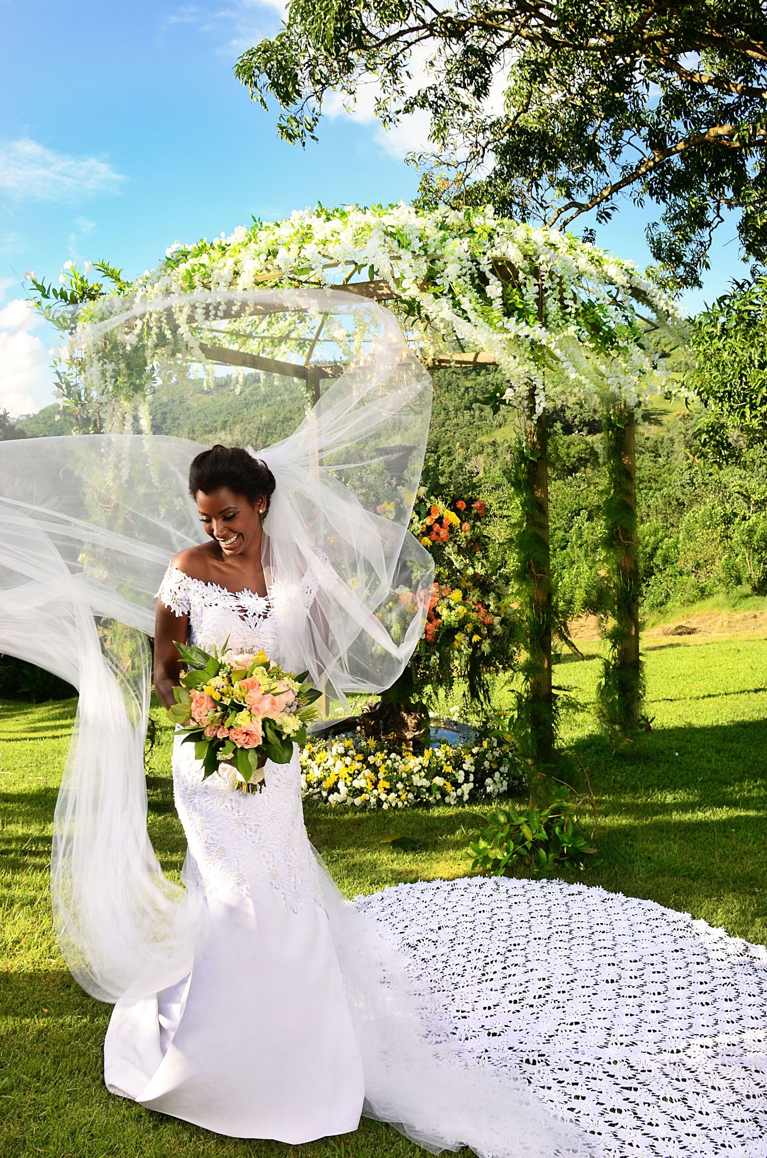 A beautiful wedding portrait under a floral arch with a flowing veil and bouquet in a garden setting.