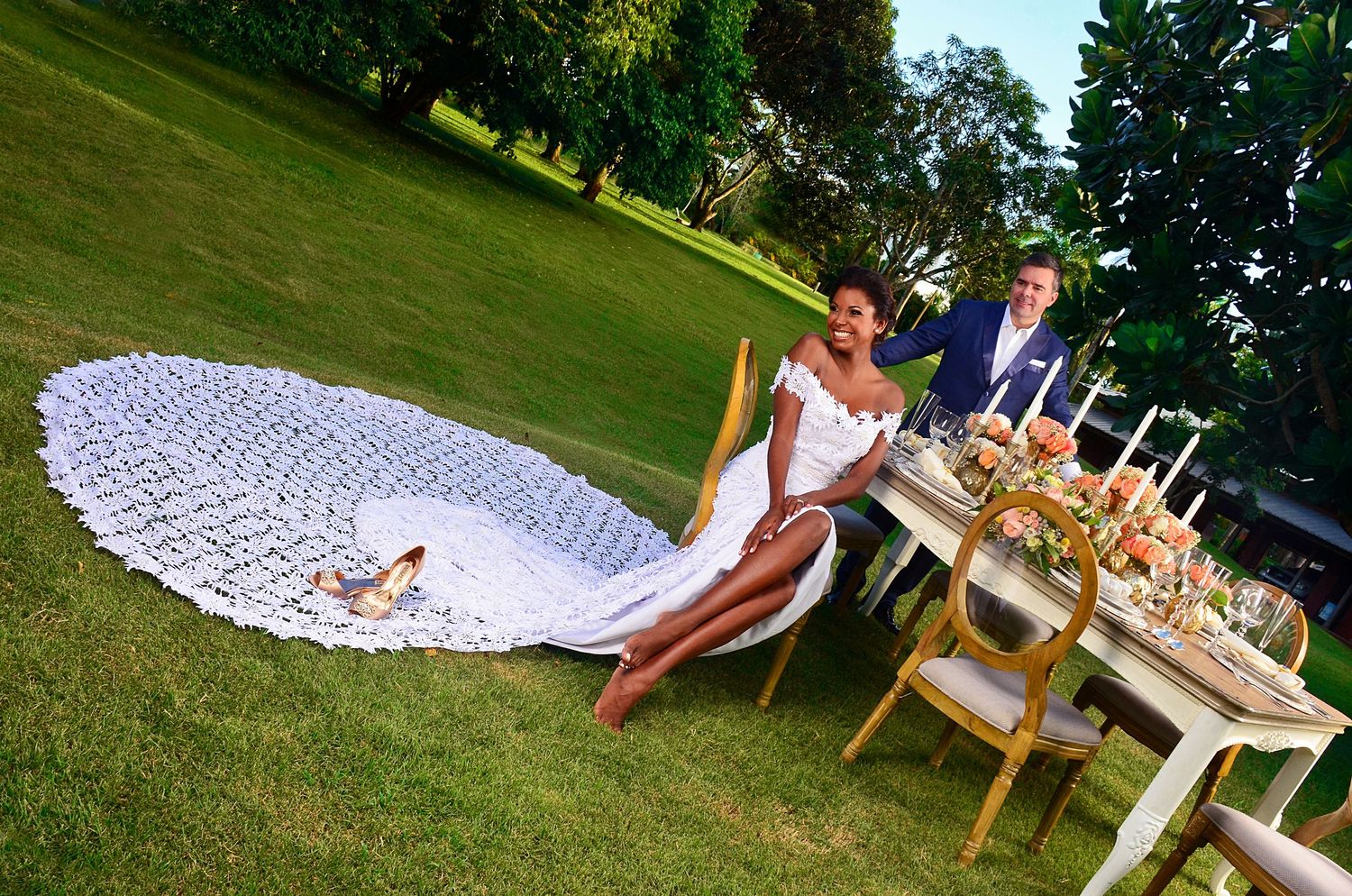 Outdoor wedding reception table setup with an elegant spread and dramatic cathedral-length train on the lawn.