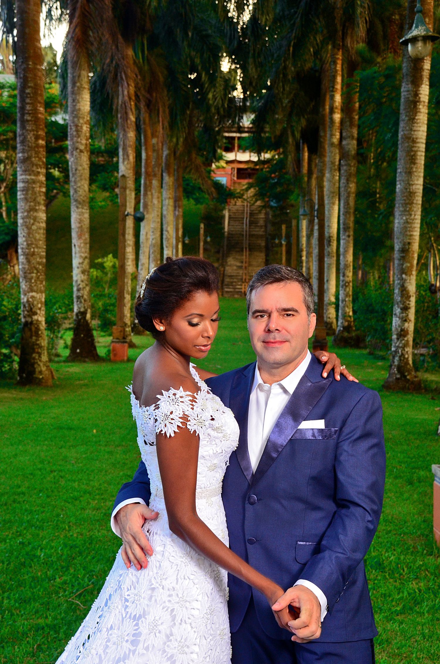 A wedding portrait set in a serene palm tree grove with lush green landscaping.