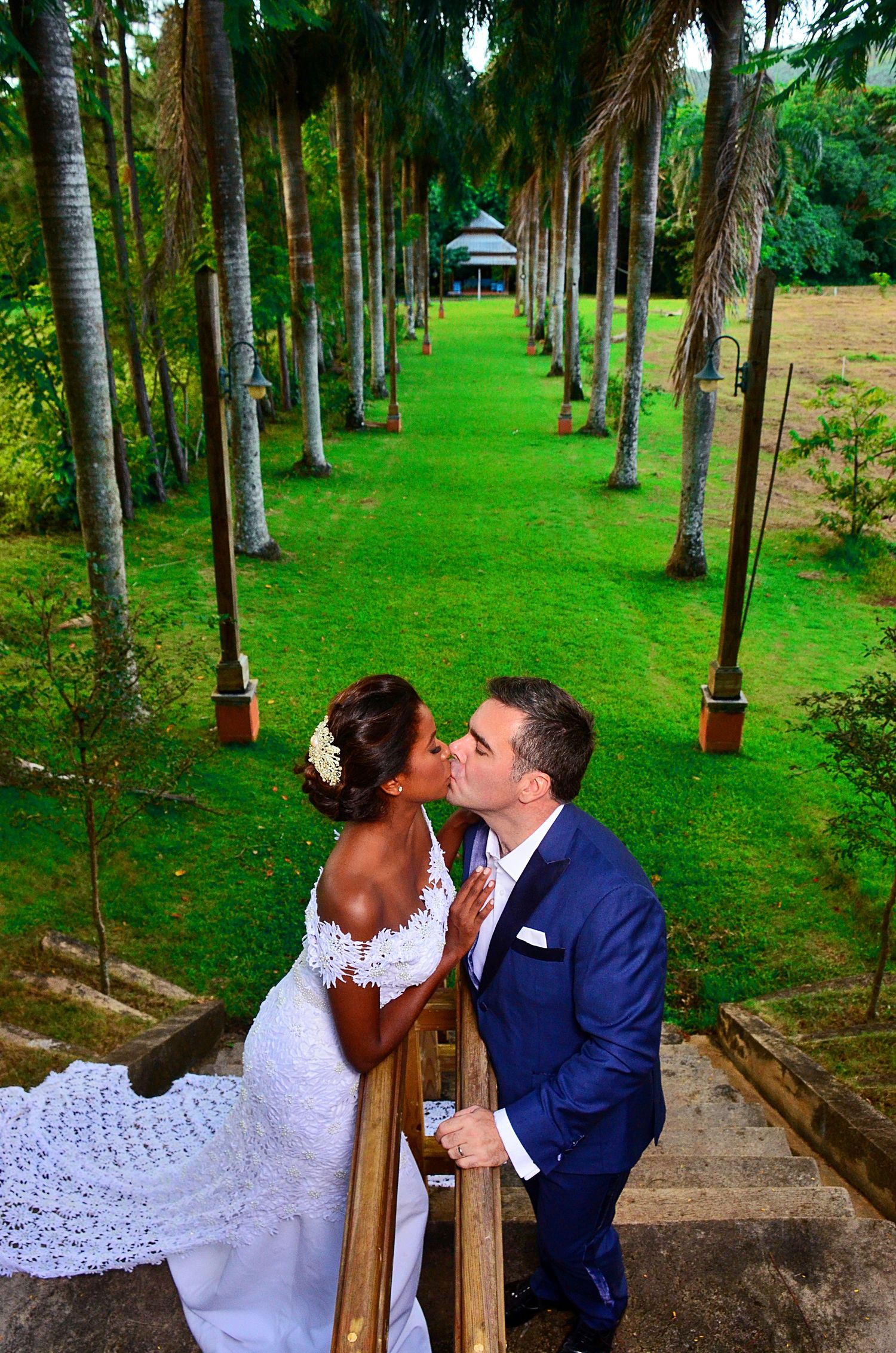 A scenic outdoor wedding moment in a palm-lined garden path with lush green landscaping.