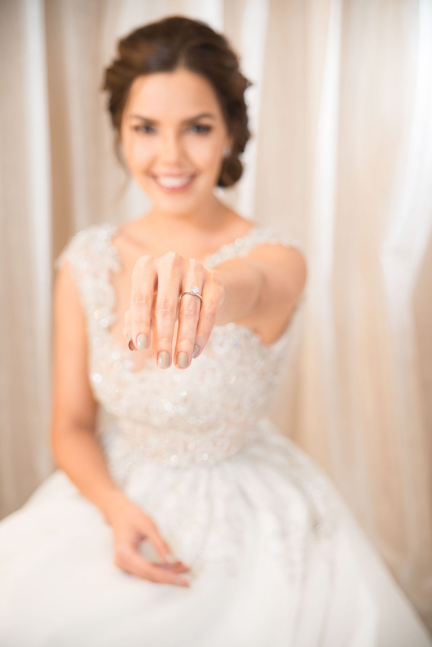 Close-up showing an engagement ring on delicate lace-adorned hand against white background.