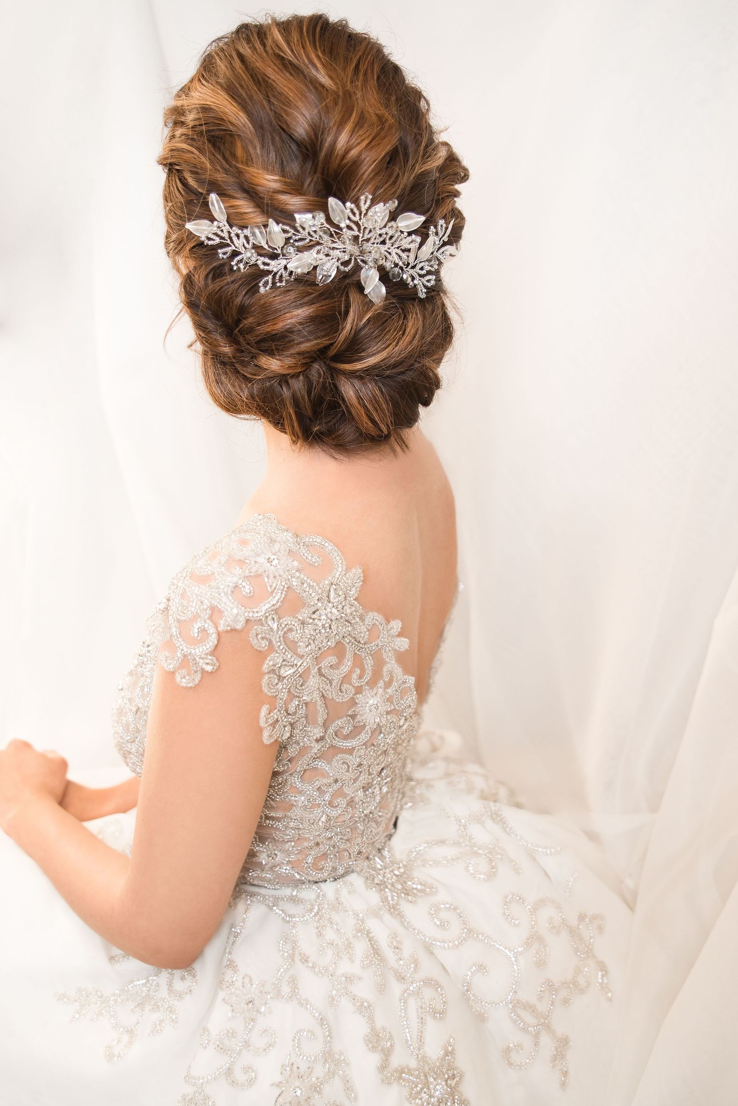 Detailed view of a bridal hairstyle with crystal hair accessory and lace-detailed dress.