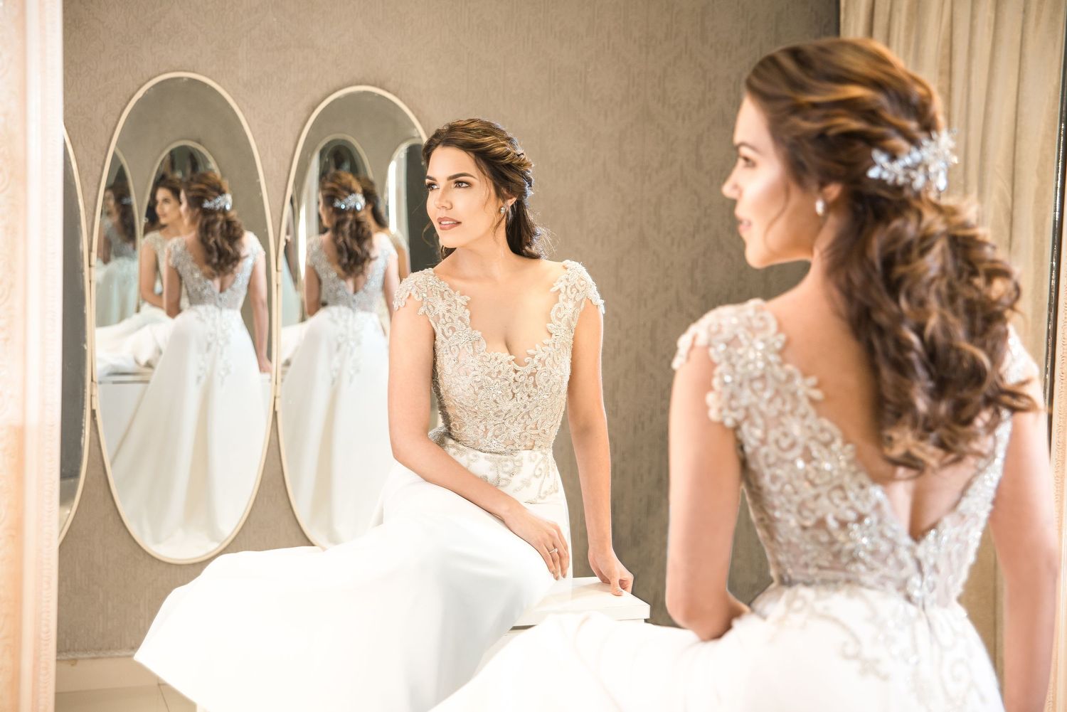 A bride's reflection multiplies in angled mirrors while showing off intricate lace details of her wedding gown.