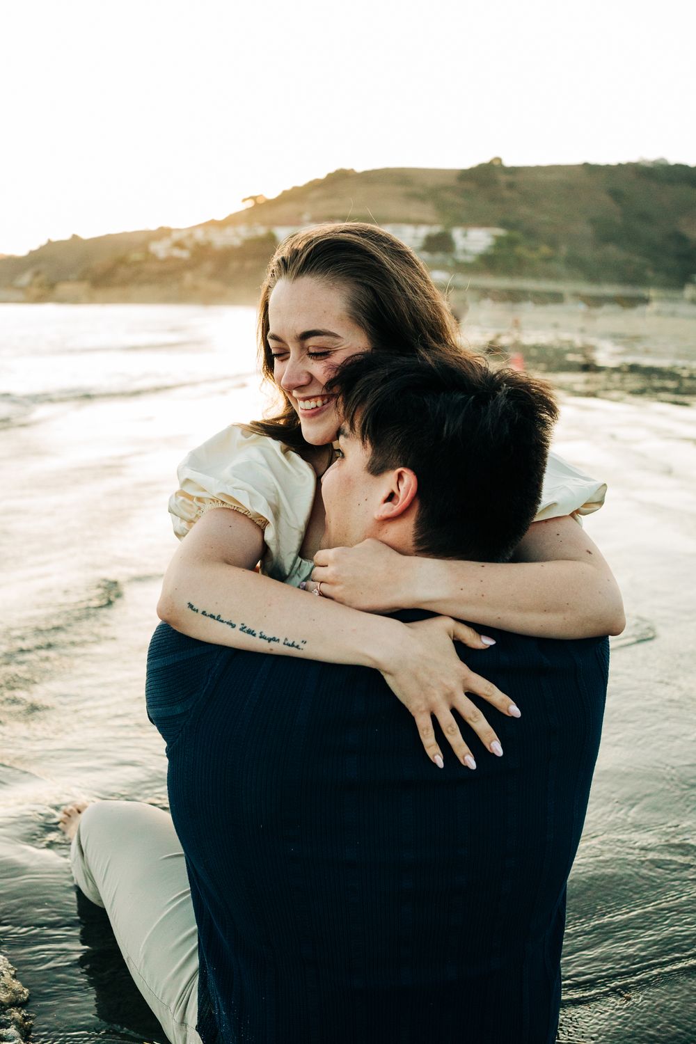 Engagement session in Pismo Beach, Ca. Man's back to the camera, fiance hugging him and looking down at the water.