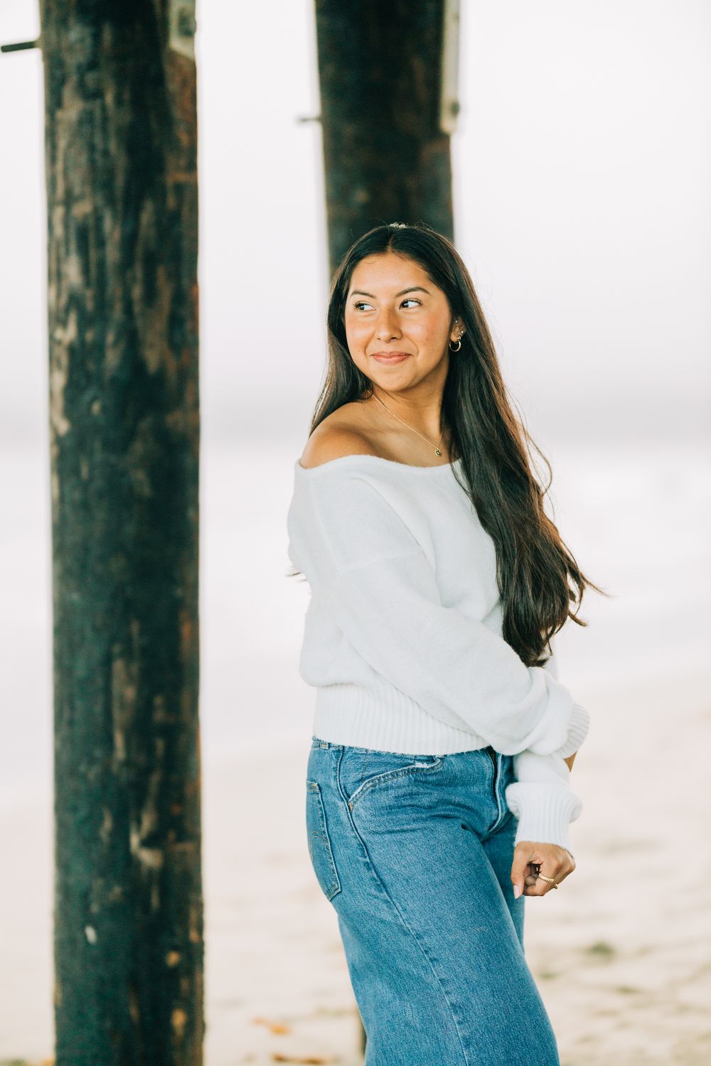 Senior girl leaning against a beam under the pier in Pismo Beach, CA.
