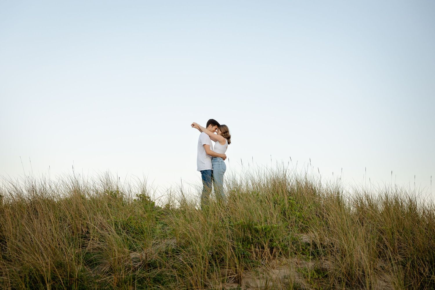 A couple embracing on a hilltop against a bright sky during golden hour on the coast in Pacific City, Oregon.