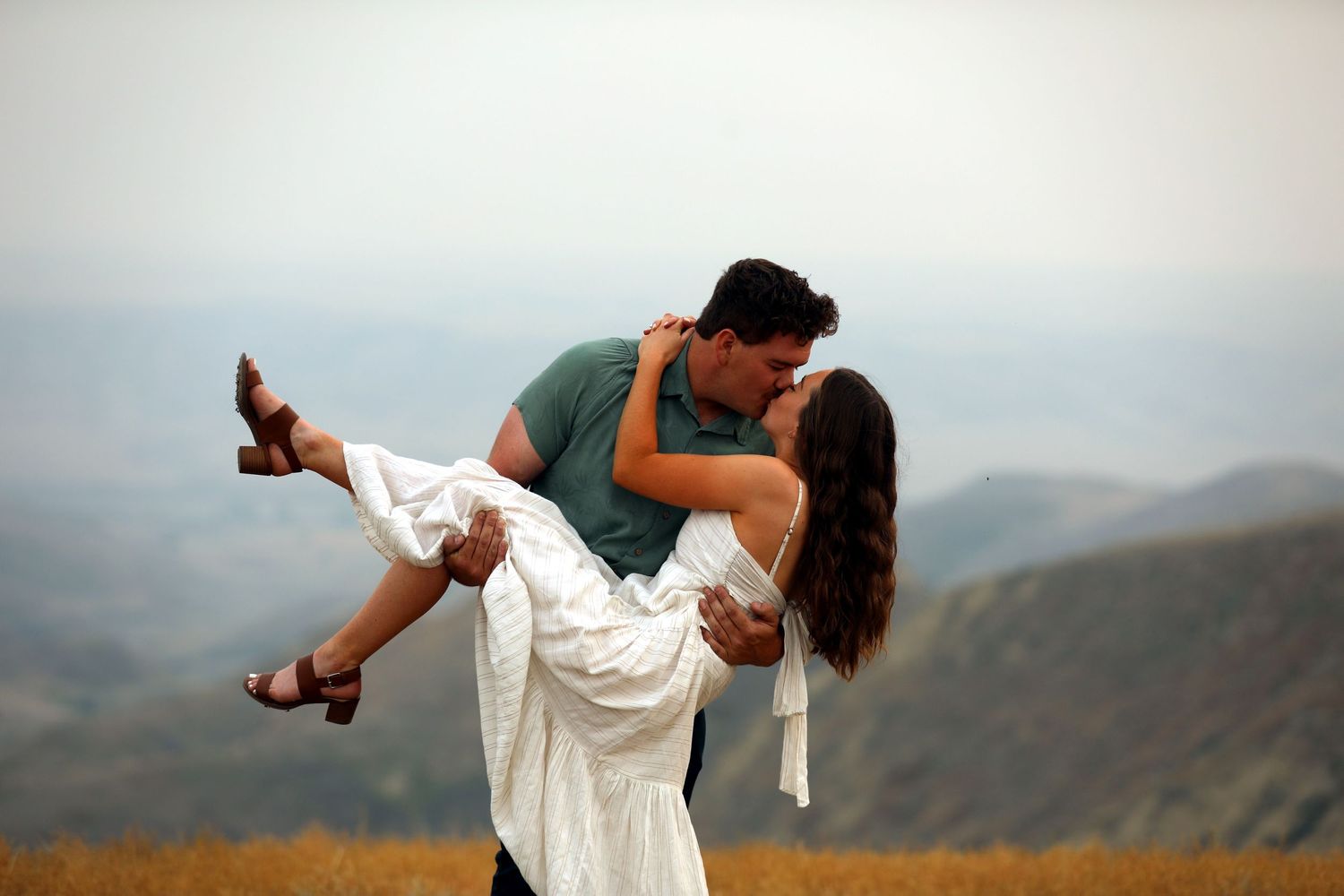 A romantic dip pose against a mountain landscape backdrop with flowing white dress.