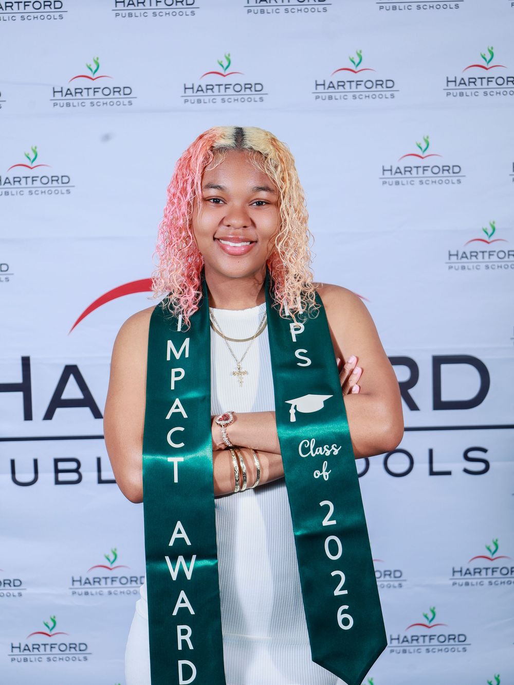 Graduate wearing a green Class of 2026 stole posing in front of a Hartford Public Schools backdrop.