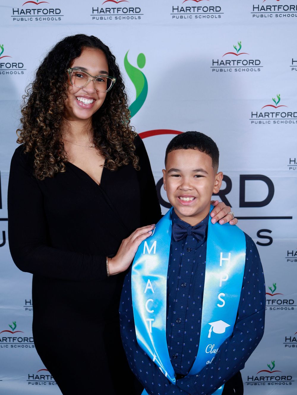 Student wearing blue graduation stole poses with mentor at Hartford Public Schools event.