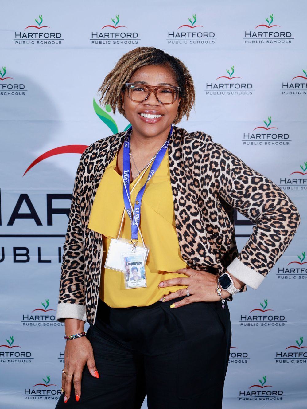 Professional wearing a yellow blouse and leopard print cardigan poses at Hartford event backdrop.
