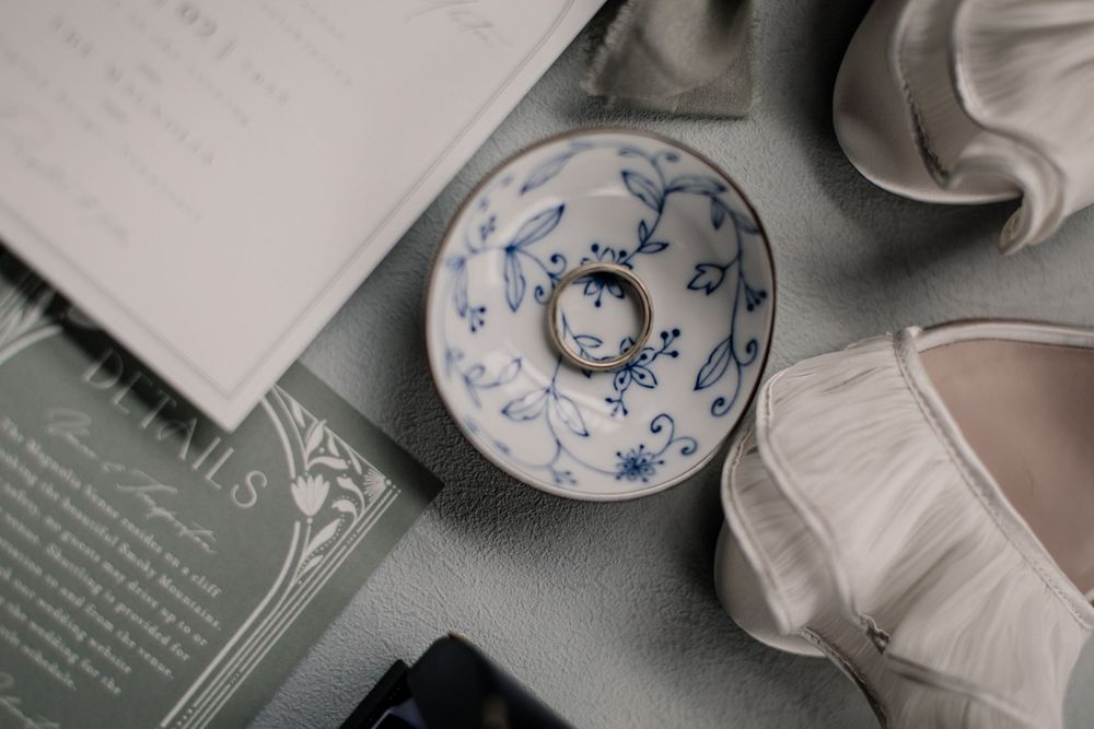 A white ceramic donut-shaped dish with delicate blue floral patterns sits among books and papers on a gray surface.