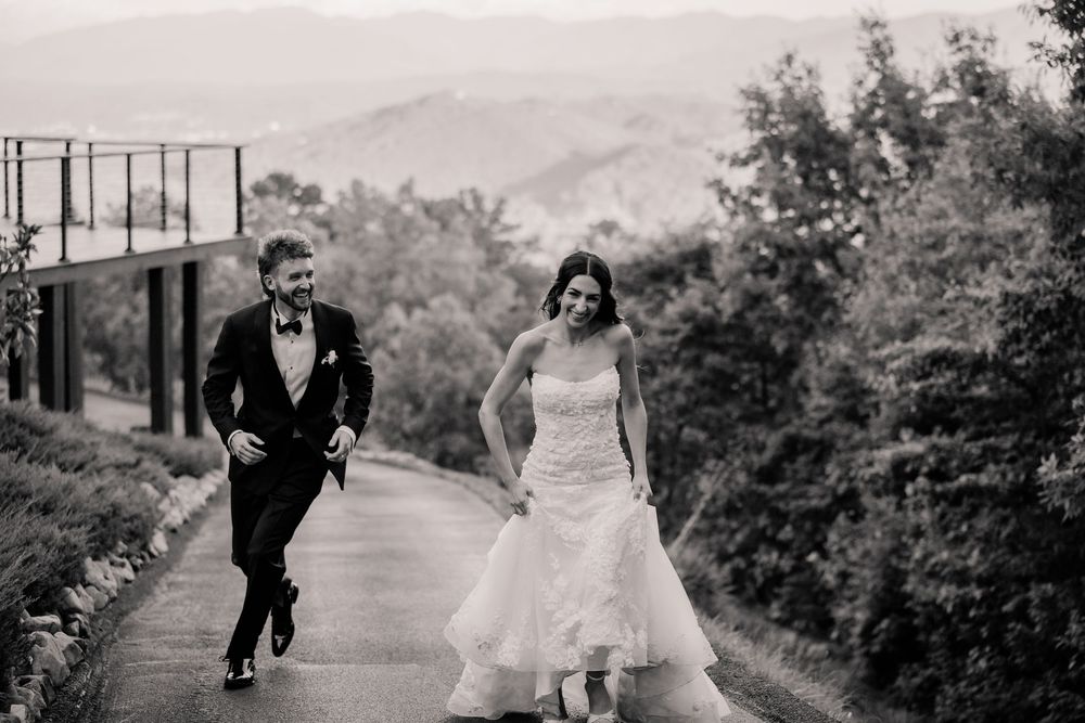 A bride and groom run playfully together on a path surrounded by lush greenery on their wedding day.