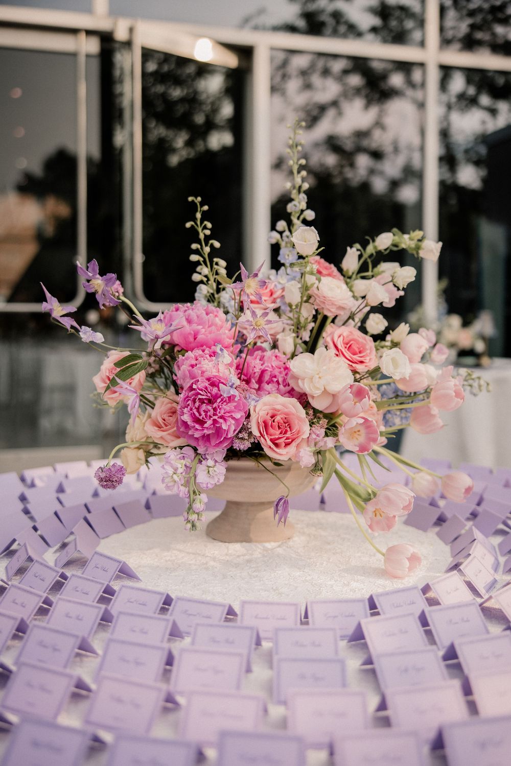 Pink and purple floral wedding escort card display with elegant rose centerpieces arranged on white tables.