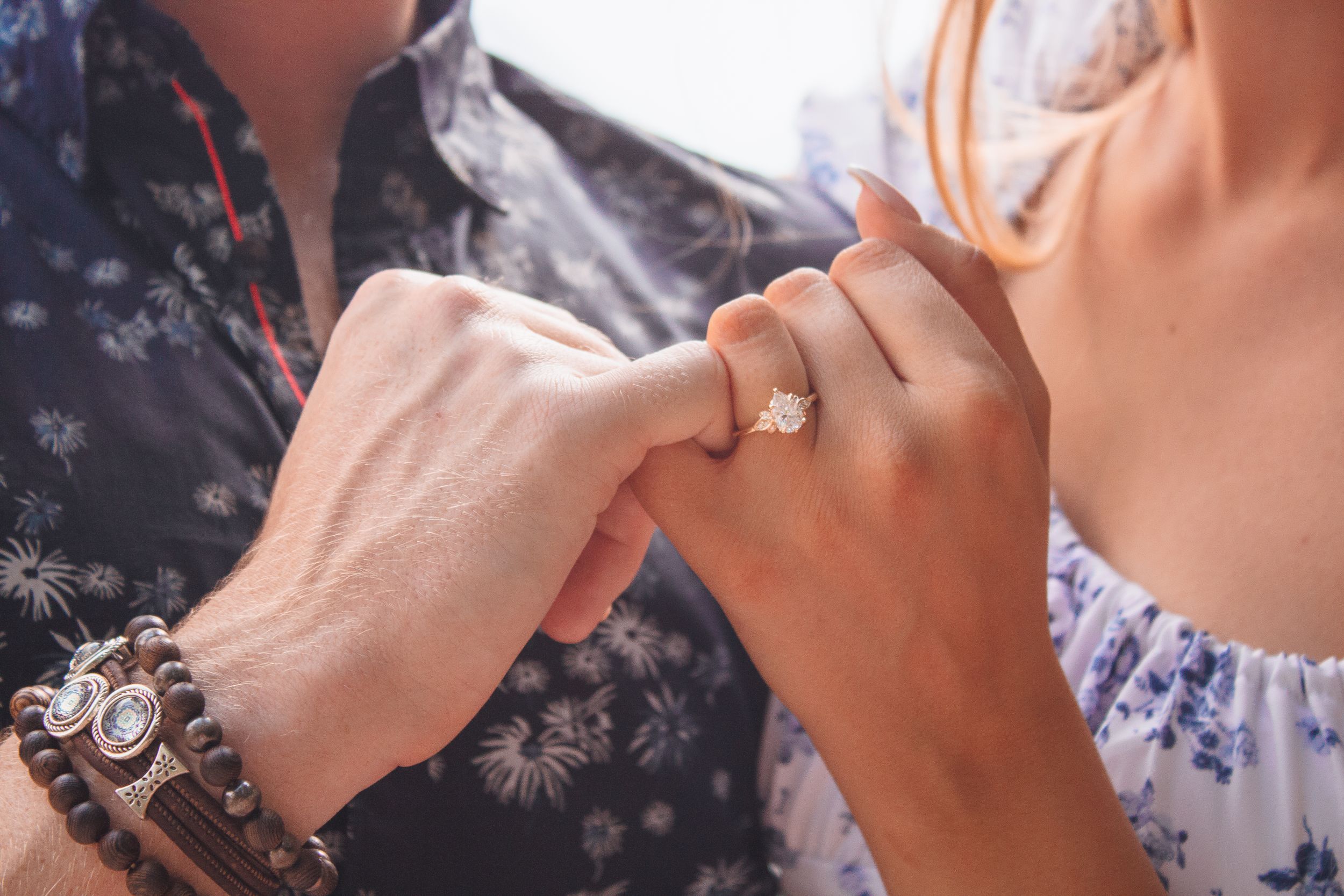 Close up of hands showing elegant diamond engagement ring with bracelets against floral printed clothing.
