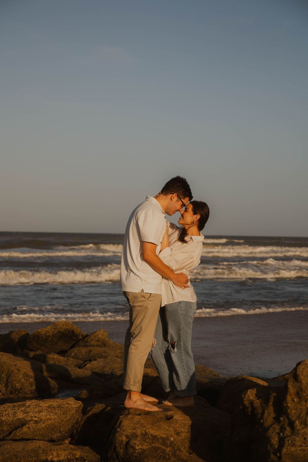 Romantic couple sharing an intimate moment on rocky beach cliffs at sunset.