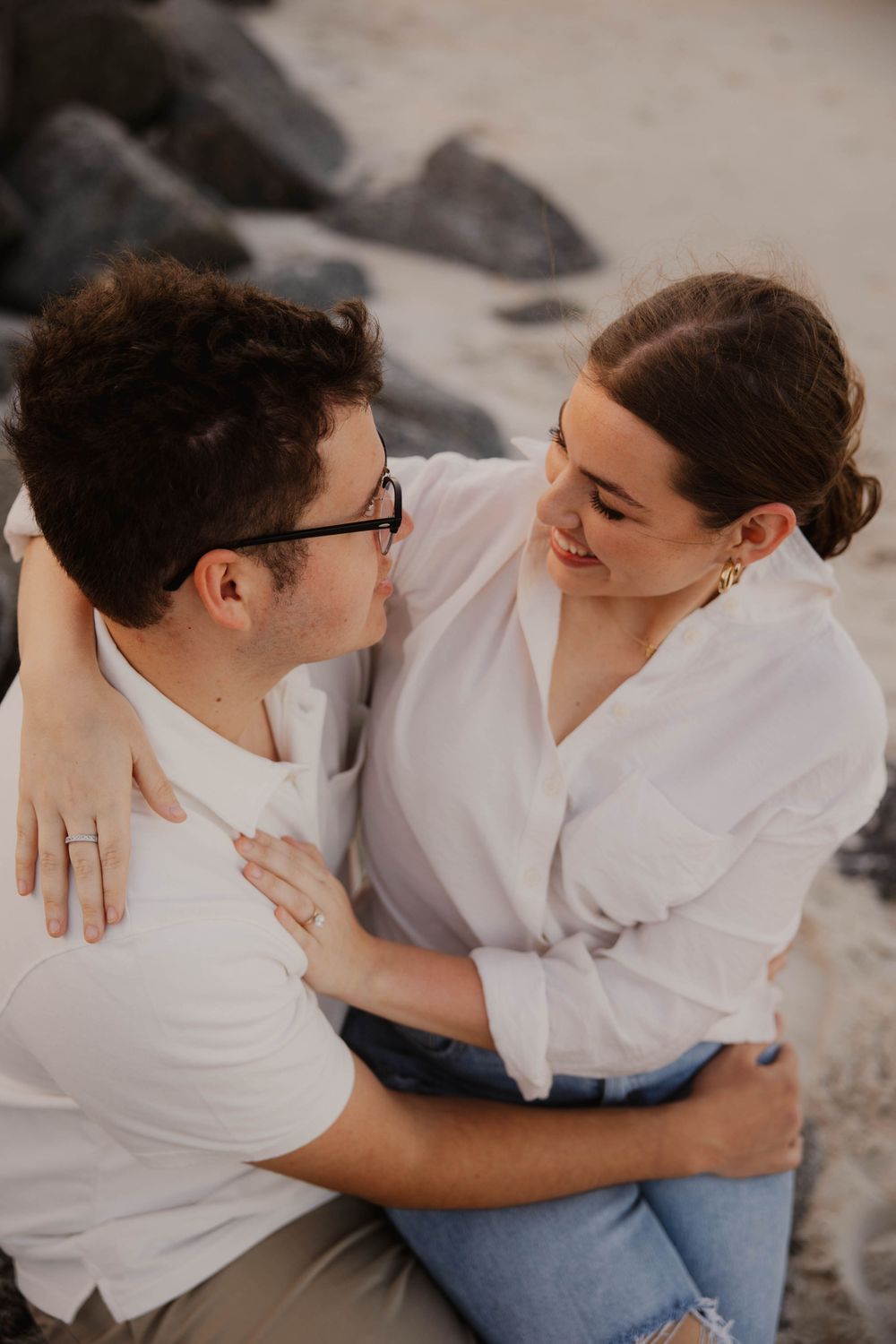 Couple in white shirts sitting close together on beach during casual photo session.