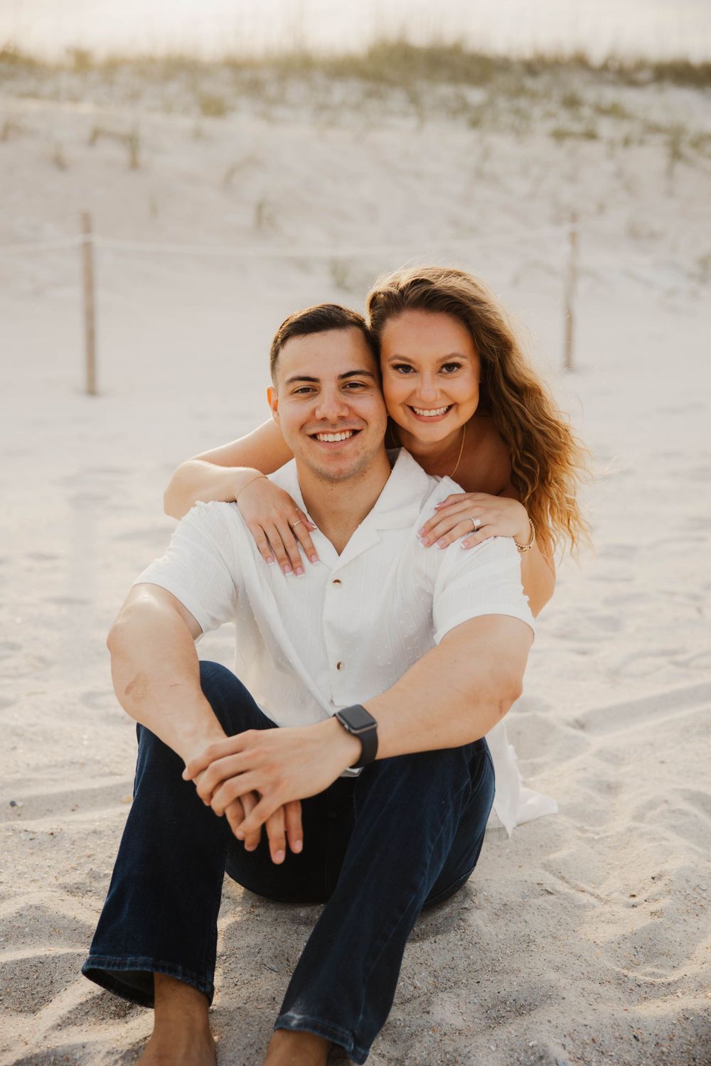 Couple in matching white tops sitting together on sandy beach.