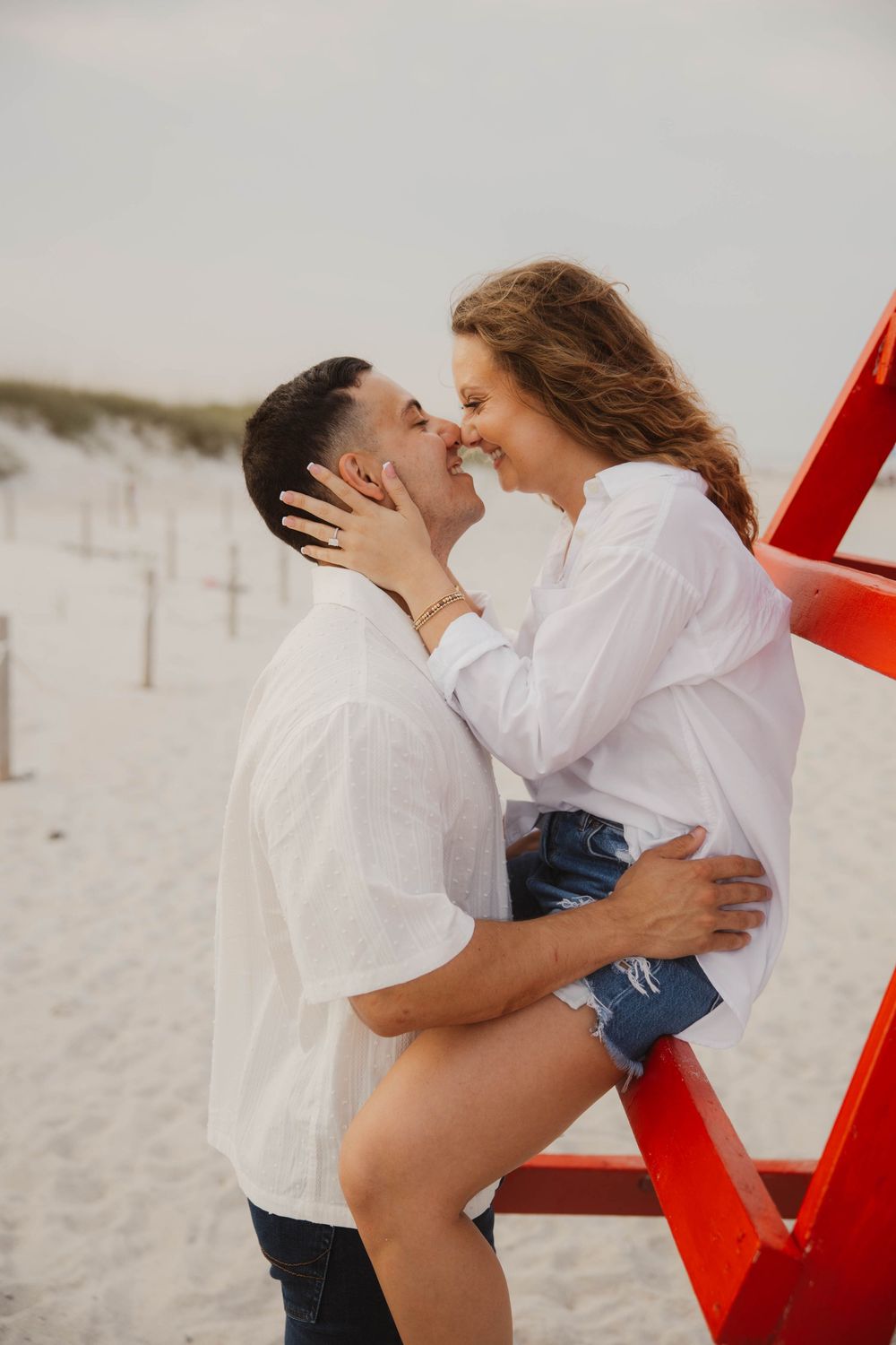 Romantic couple photos by red lifeguard stand showing intimate moments.