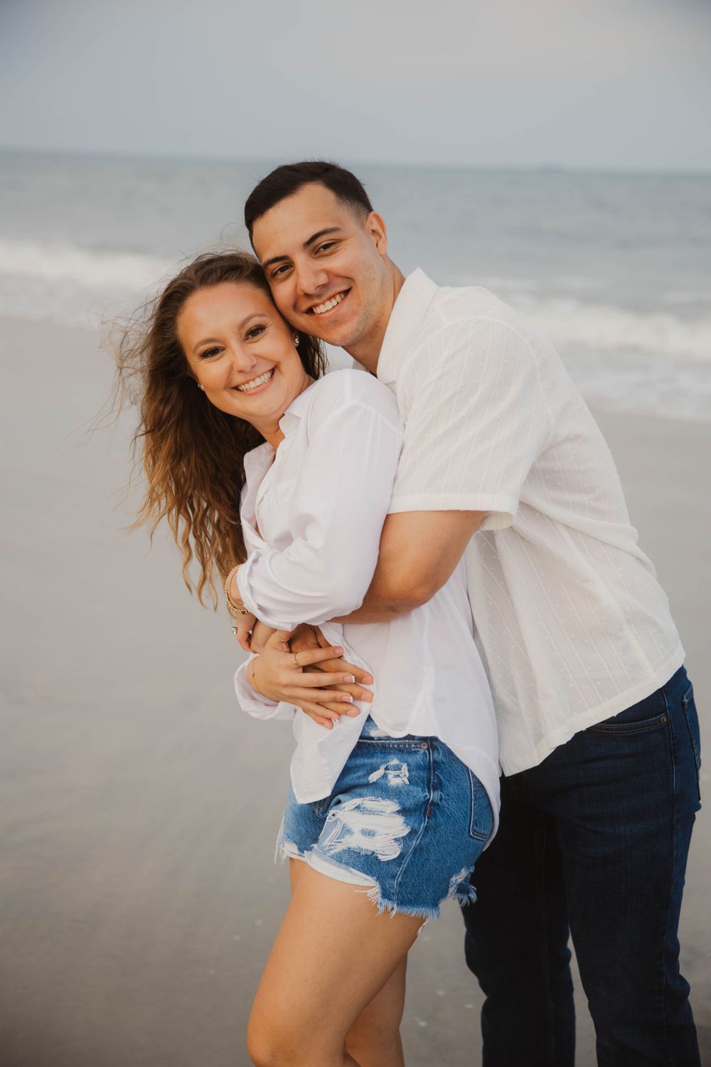 Playful beach portraits of couple in white shirts and denim.