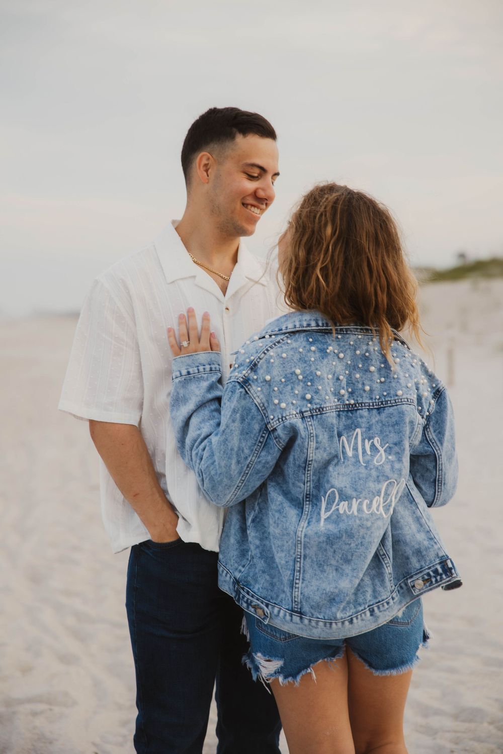 Couple in coordinated outfits with custom denim jacket on beach.