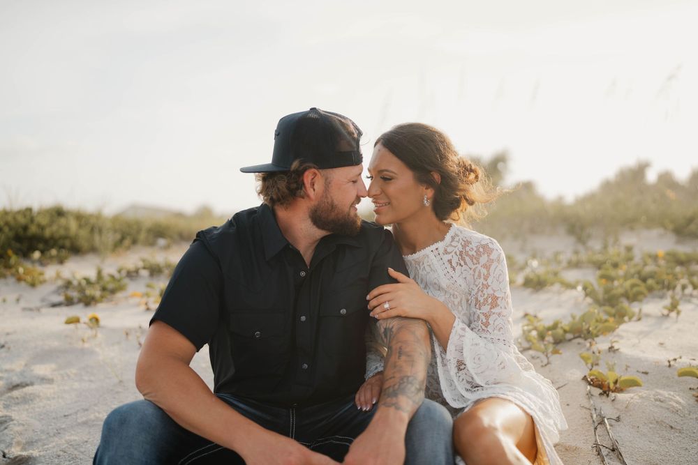Couple shares intimate moment while sitting together on sandy beach at sunset.