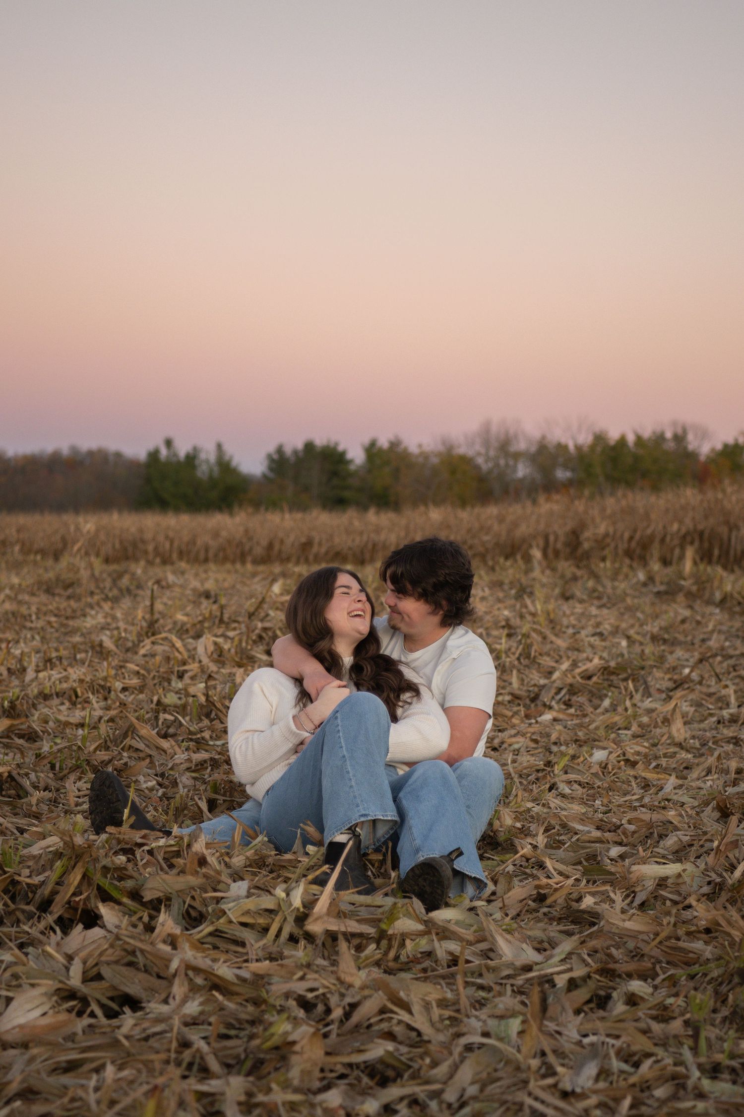 Two people sit together intimately in a harvested cornfield at sunset creating a romantic rural scene.