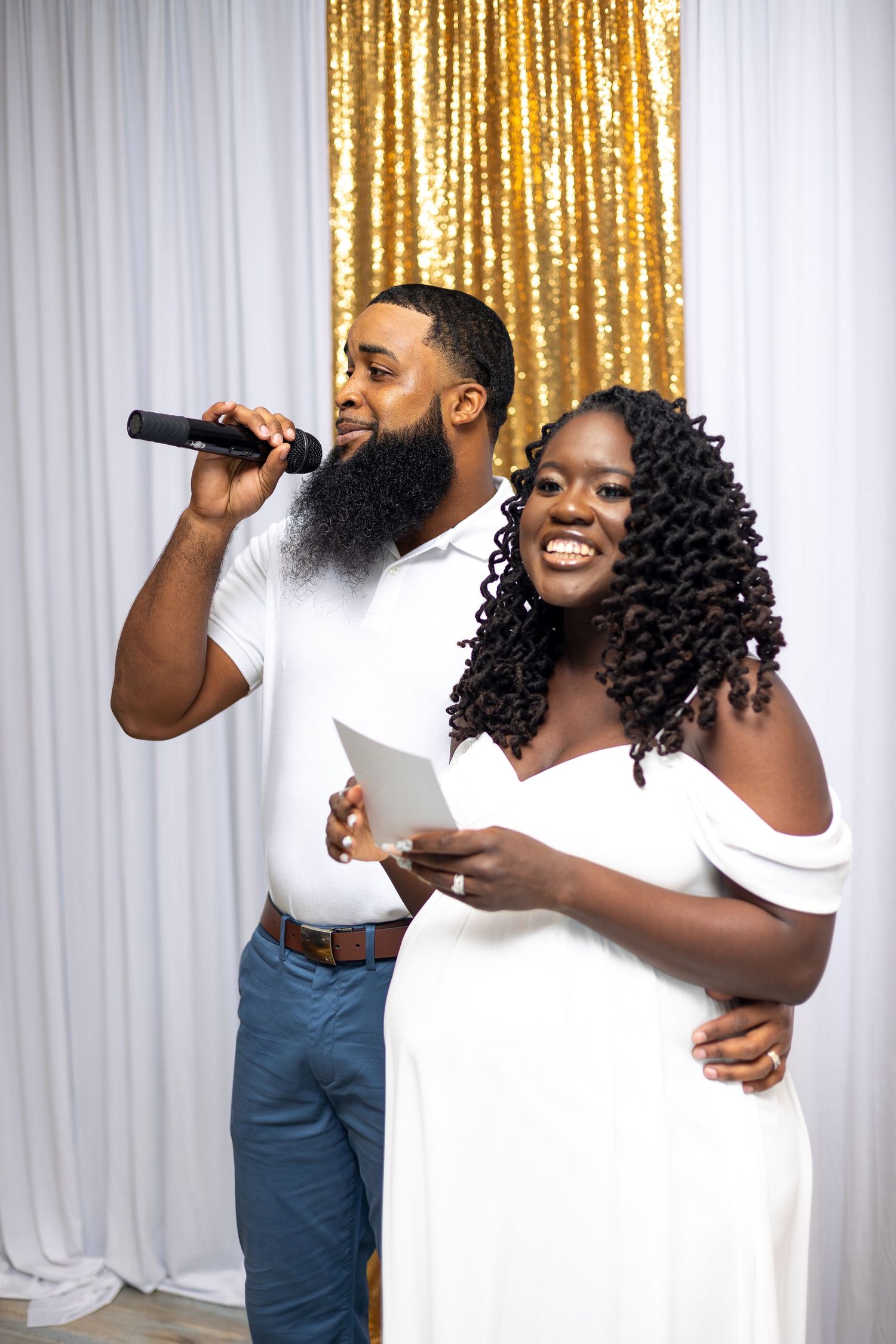 Two people in white outfits performing against gold sequin backdrop.