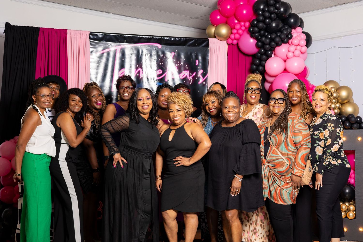 Group celebration photo with pink and black balloon decorations and party attire.
