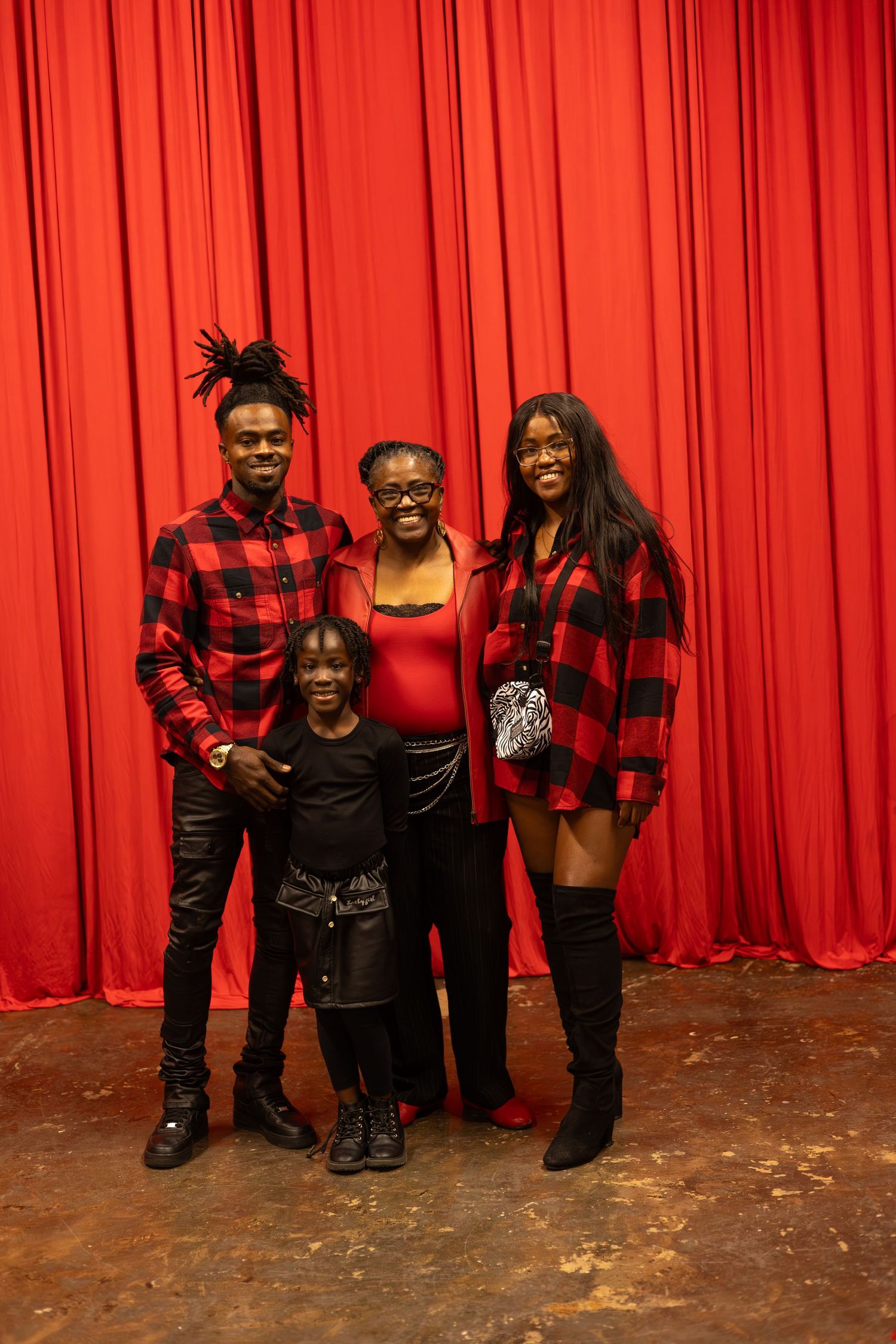 Group wearing matching buffalo plaid outfits poses in front of red curtain backdrop.