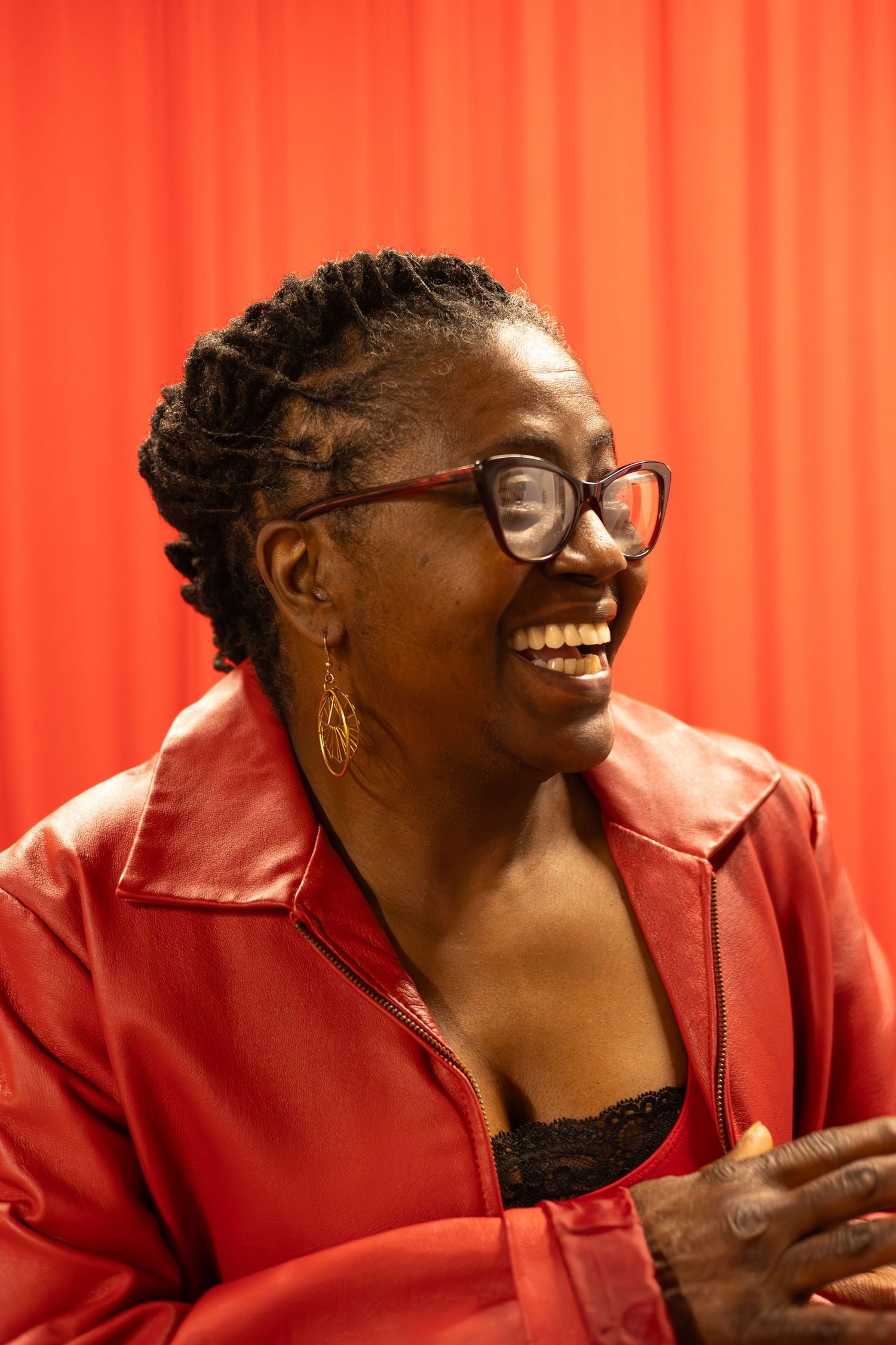 Person in red leather jacket laughing joyfully against vibrant red background.