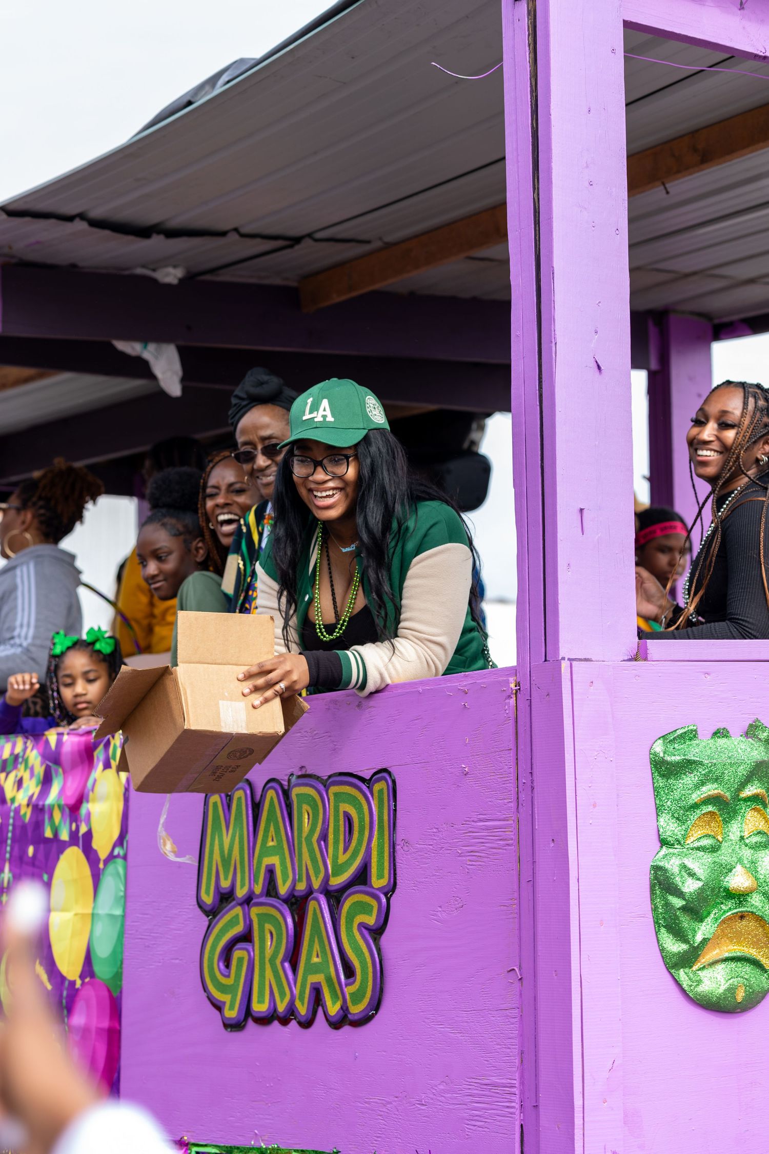 People celebrate on purple Mardi Gras float decorated with festive masks and beads.