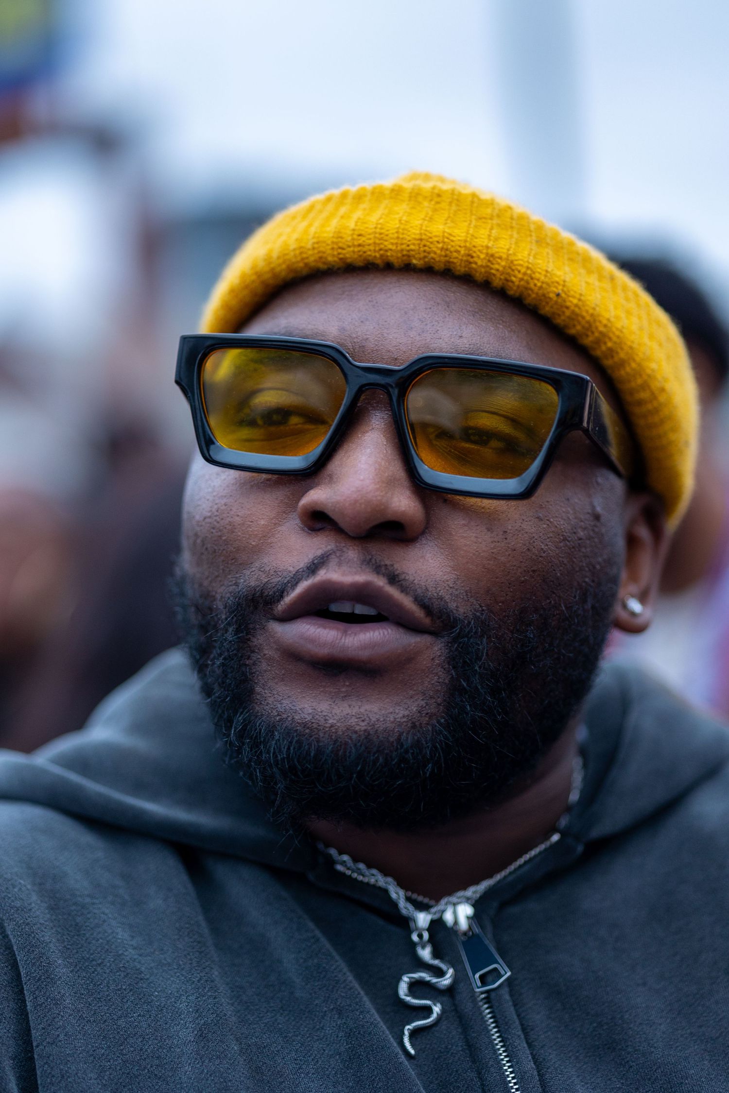 Person wearing yellow beanie and black glasses at outdoor event.