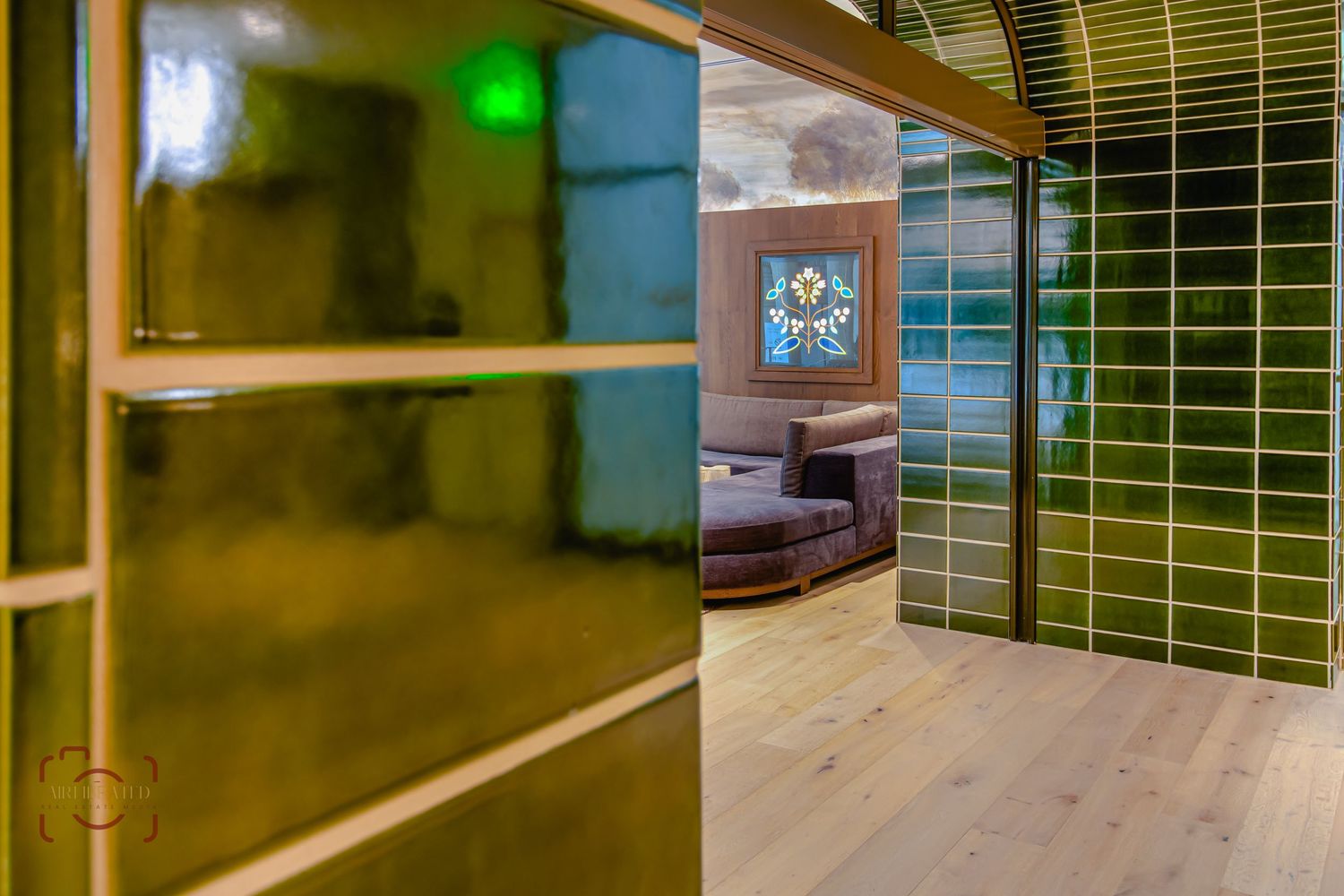 Modern office corridor with green tile wall and wooden flooring leading to a seating area.
