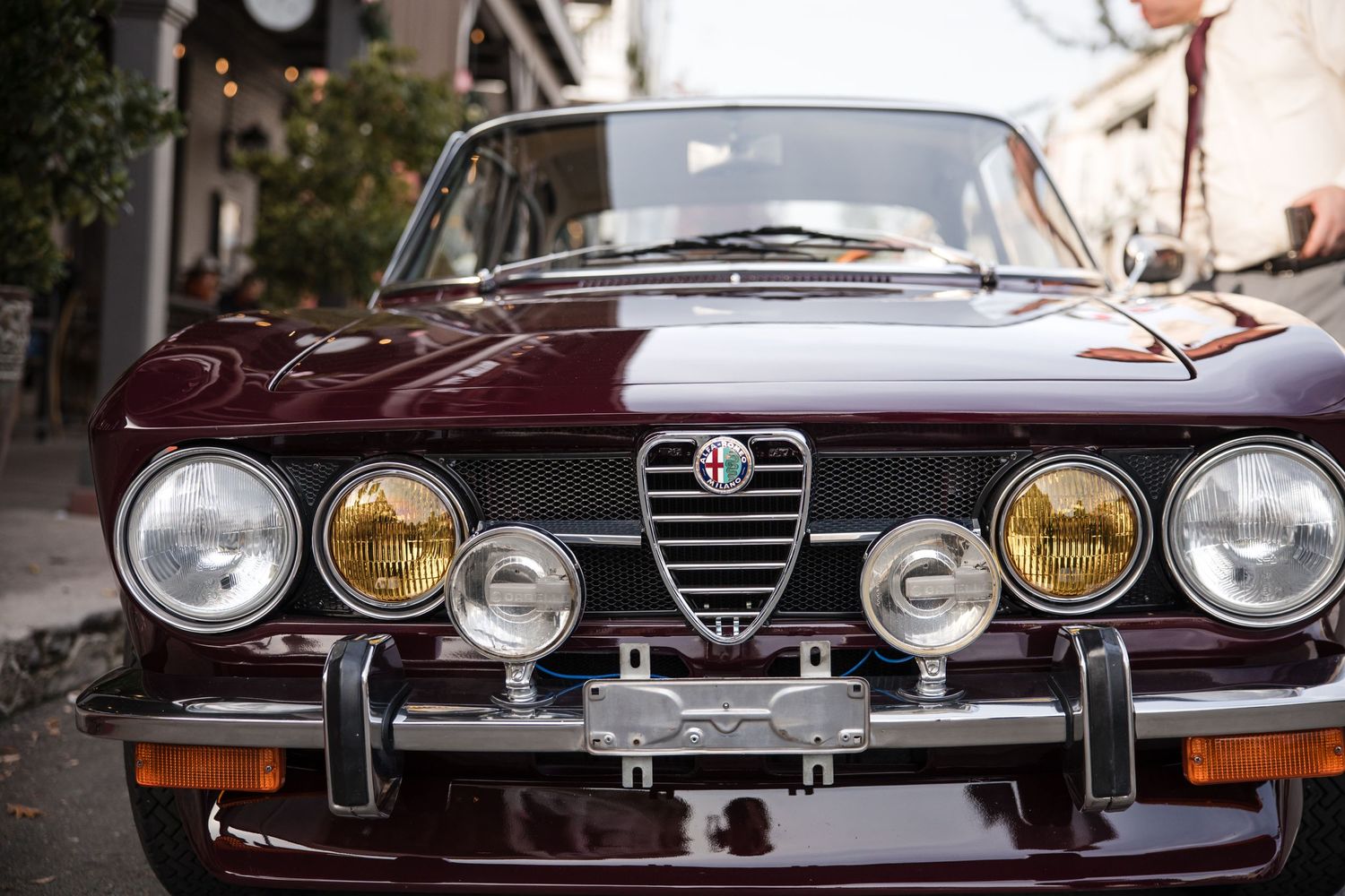 Close-up of a vintage burgundy Alfa Romeo car front with round headlights and iconic grille.