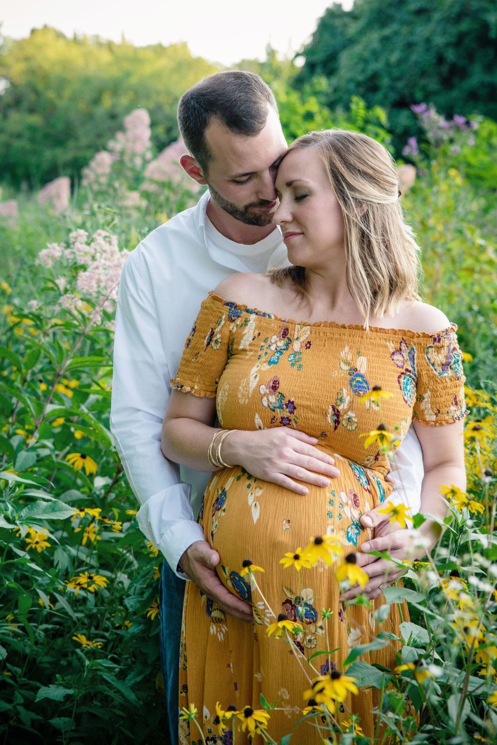 Pregnant woman in yellow floral dress with partner in outdoor garden maternity photoshoot at sunset.