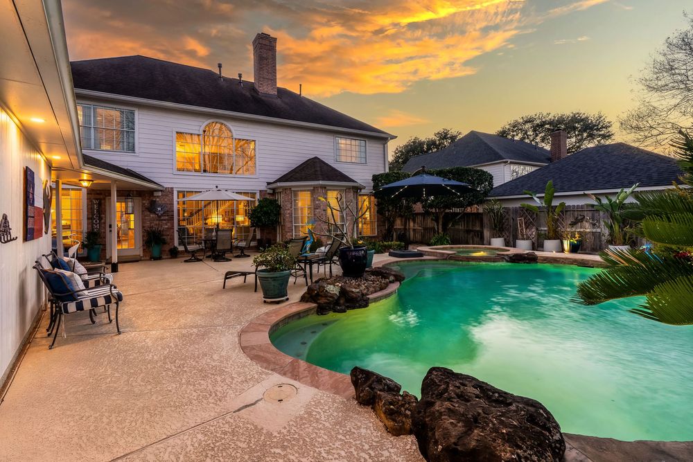 A panoramic view of a luxury resort pool area at sunset with glowing lights and tropical landscaping.