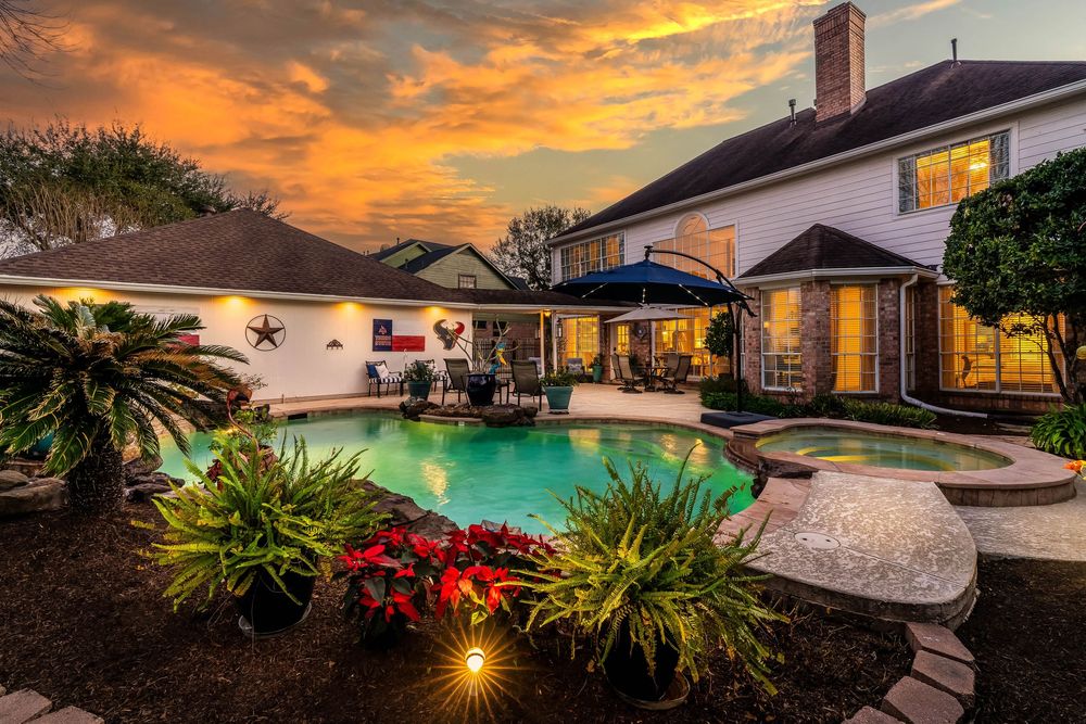 Stunning sunset panorama over residential homes with dramatic orange and purple clouds reflecting in a backyard pool.