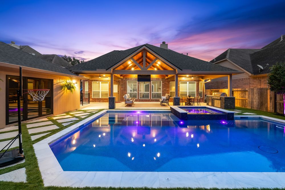 Luxury backyard pool with glowing blue lights, covered patio, and outdoor seating at twilight.