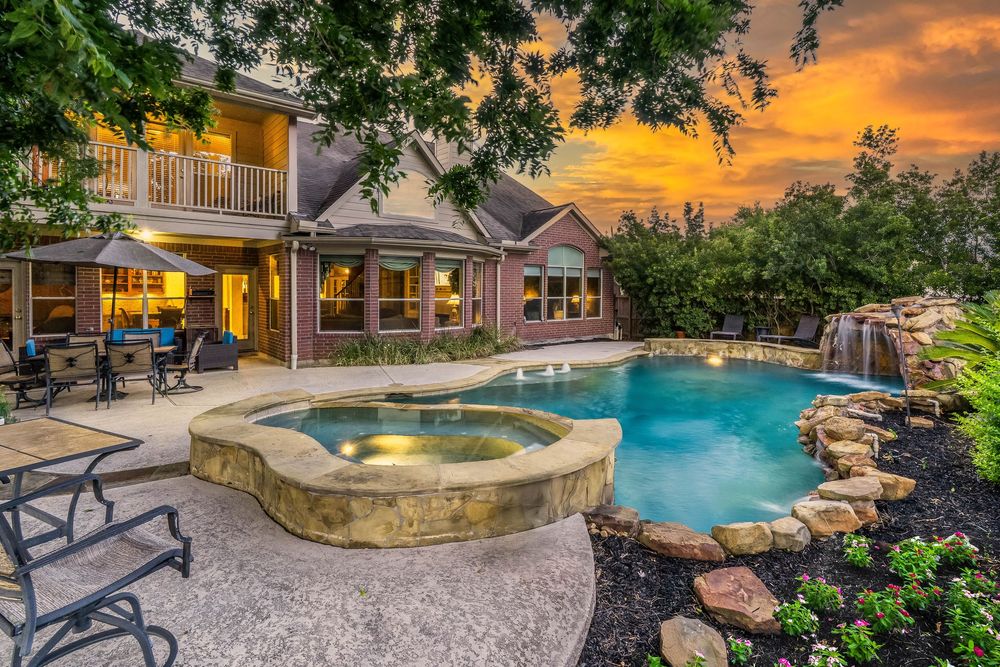 Luxurious backyard pool and hot tub with natural stone features against a stunning orange sunset sky.