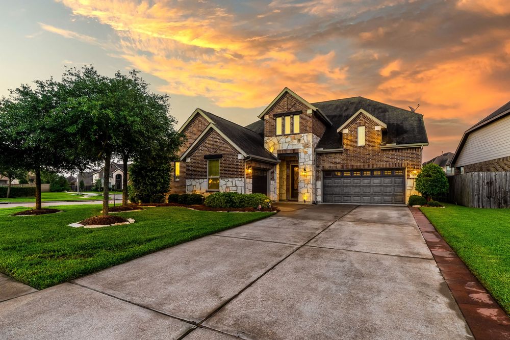 Beautiful two-story brick home with dramatic sunset sky and manicured lawn viewed from the driveway at twilight.